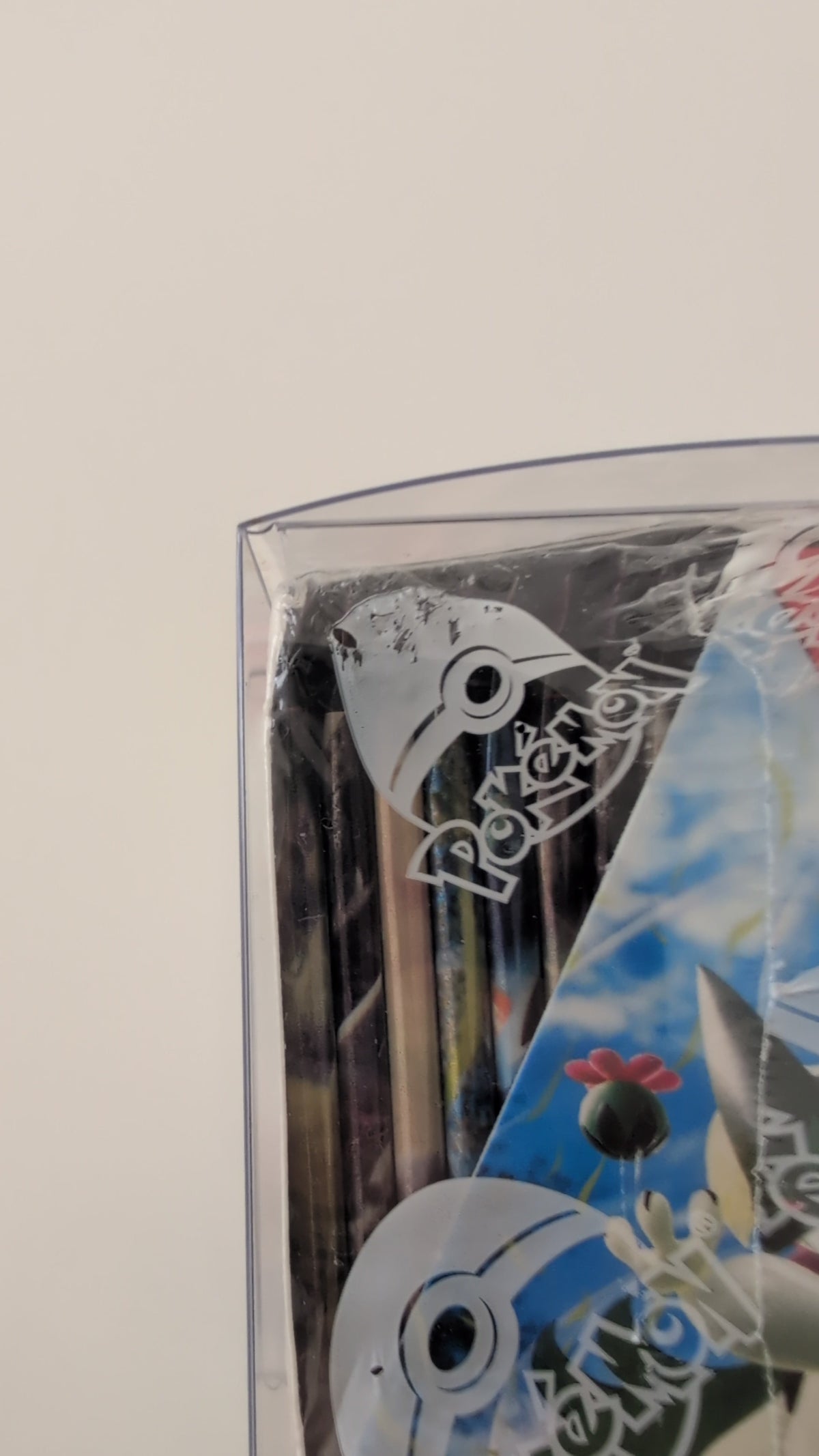 A close-up of a clear plastic pouch containing Pokémon-branded printed items, including a blue illustrated card or sticker with a Pokémon logo and character artwork, against a plain light background.